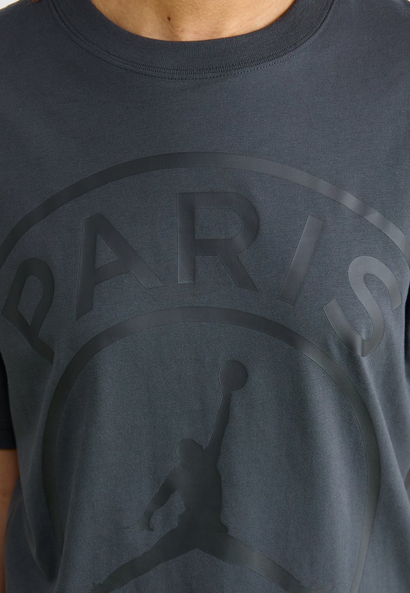 Dunkelgraues T-Shirt aus Baumwolle, mit einem großen, mattschwarzen "PARIS"-Text und einer Silhouette eines Spielers in Aktion unter dem Text.