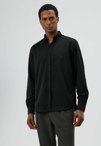 Zwart lang mouwen overhemd met knopen, gemaakt van gladde stof, voorzien van een puntige kraag en een subtiel gebogen zoom, gedragen met grijze broek.