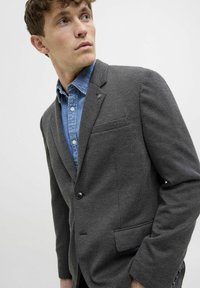 Grauer Hahnentritt-Blazer mit Revers, einreihiger Knopfverschluss und Taschen, getragen über einem blauen Denimhemd. Dezente Textur und Muster.