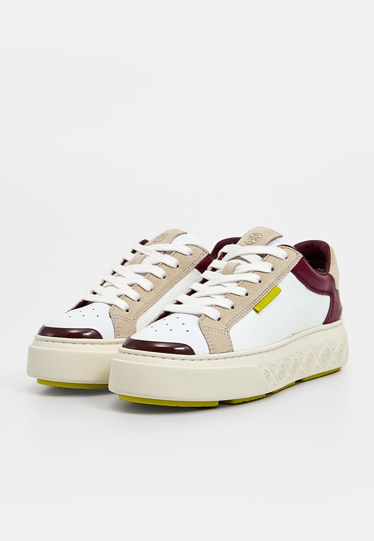 Weiße Sneaker mit beigen Wildleder-Akzenten, burgunderfarbenem Fersenbereich und strukturiertem cremfarbenem Plateau. Mit gelbem Logo-Tag und perforiertem Zehenbereich.