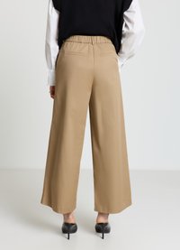Beige Hosen mit weitem Bein und elastischem Bund, glatter Textur, seitlichen Taschen und Gesäßtaschen, kombiniert mit schwarzen High Heels.