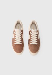 Sneakers in suede marrone con dettagli e lacci bianchi, caratterizzati da una punta arrotondata e una finitura testurizzata. Logo visibile sulla linguetta.