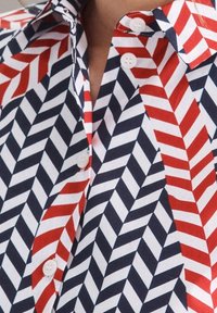 Knapplång skjorta med ett iögonfallande chevronmönster i röd, marinblå och vit. Tillverkad av lätt tyg med en mjuk textur och klassisk krage.