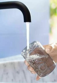 Zwarte gebogen kraan die water in een helder glazen pot giet. De pot heeft een gestructureerd oppervlak met luchtbelletjes en een ronde ingedrukte detail.