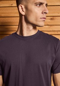 Camiseta de manga corta de color púrpura oscuro, hecha de una tela suave y ligera, con cuello redondo y detalles de costura limpios.