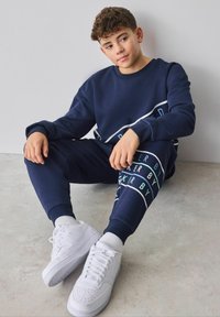 Marineblaues Sweatshirt und Jogginghosen-Set mit weißen und aqua-farbenen Grafiken; kombiniert mit weißen Turnschuhen. Weicher Stoff und entspannte Passform.