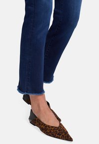 Baleriny w panterkę ze spiczastym noskiem i czarnymi skórzanymi akcentami, noszone z ciemnoniebieskimi dżinsami o postrzępionych nogawkach u kostek.