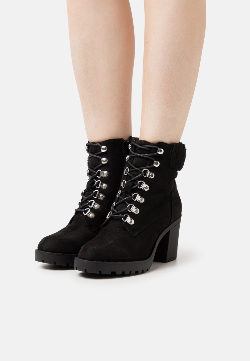 Bottines en daim noir avec un devant à lacets, quincaillerie argentée, col texturé et un talon épais. Semelle en caoutchouc avec des détails de bande de traction.