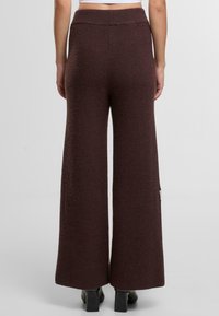 Kalhoty s širokým nohavicí v tmavě hnědé texturované tkanině, s elastickým pasem a detaily v bočním švu, navrženy pro uvolněný střih.