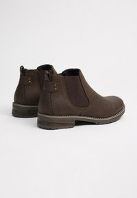 Par de botas Chelsea de cuero marrón con paneles laterales elásticos, tiradores y tacones bajos apilados sobre un fondo blanco.