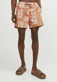 Zwemshorts in licht perzikkleur met witte geometrische patronen, voorzien van een elastische tailleband en een trekkoord. Draag ze met bruine instapsandalen.