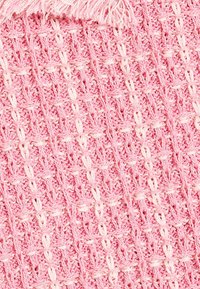 Rosa vævet tekstil med et krydsmønstret design, der har hvide accenter og frynset kanter. Teksturen fremstår blød og hyggelig.