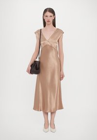 Satin midi kjole i lys gull med v-hals, kortermede ermer og rynket midje. Kombinert med en strukturert svart håndveske og hvite høye hæler.