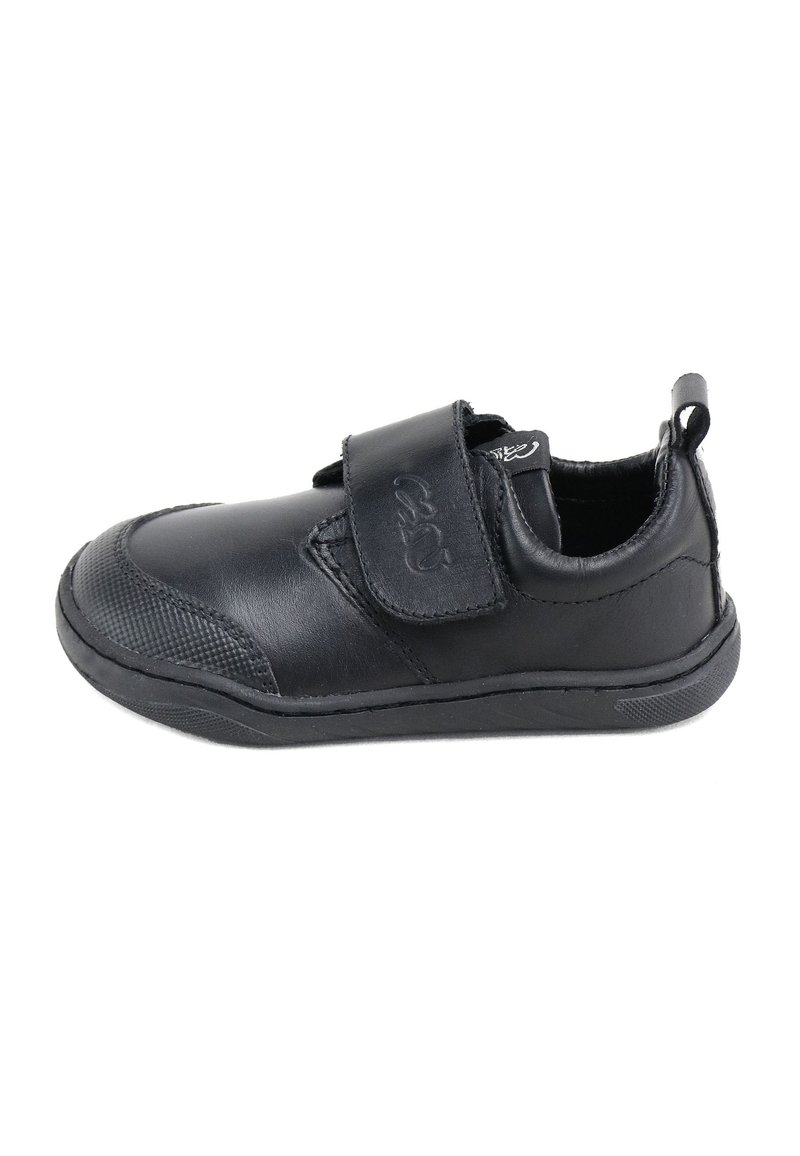 Zapato sintético negro con puntera redondeada, correa de velcro, capucha texturizada en la punta y suela plana de goma. Incluye una pestaña en el talón para facilitar el calzado.