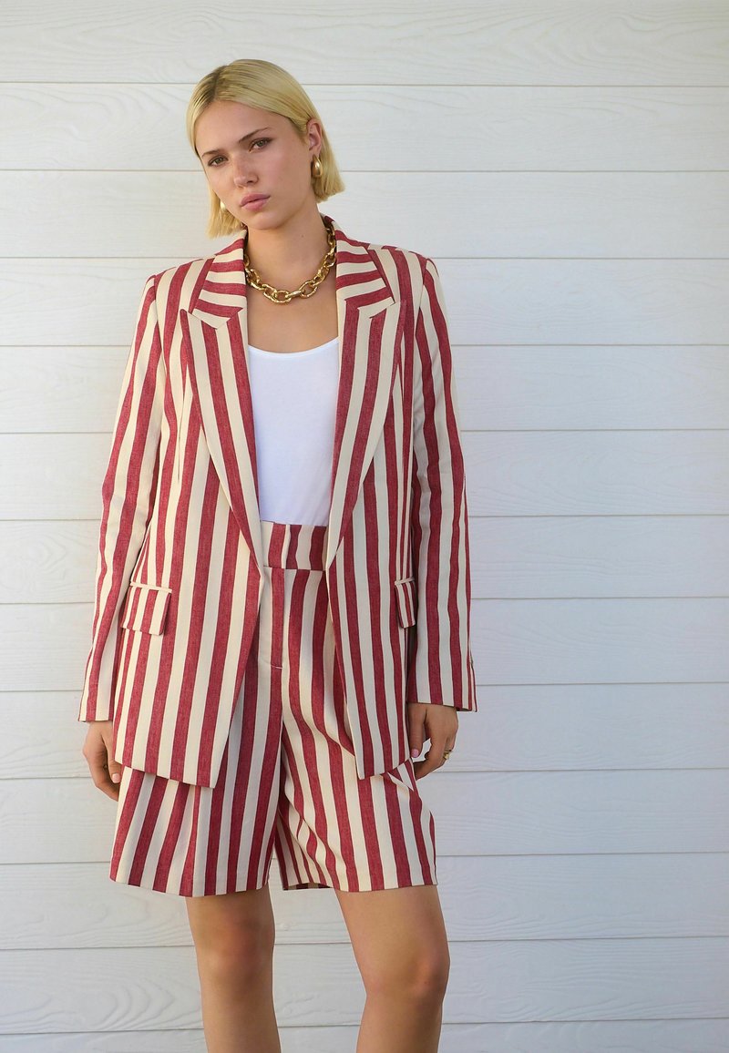 Blazer rayé rouge et crème avec un short assorti. Comprend des revers structurés, des poches avant et une texture de tissu lisse.