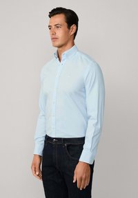 Camicia azzurro chiaro con bottoni, a maniche lunghe, realizzata in un tessuto morbido. Presenta un piccolo logo sul petto e un design di colletto classico.