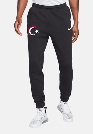 Uomo che indossa joggers neri con motivo a mezzaluna e stella bianca e logo Nike, abbinati a sneaker bianche Nike Air 270.
