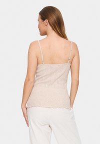 Beez tank top pehmest kangast, reguleeritavate rihmadega, tekstuurse mustriga ja lainelise servaga, koos heledate pükste pari.
