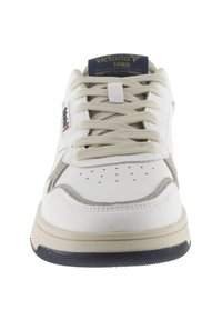 Sneaker bas blanc avec des lacets beiges, bout perforé et un accent en suède gris. Présente une étiquette bleue et blanche sur la languette.