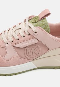 Tuviena rozā Michael Kors sporta apavi ar bēšām šņorēm, teksturētu audumu un zaļganu rakstainu mēli, kurā ir MK logo.