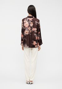 Σκούρο φλοράλ μπλουζάκι με ανοιχτό ροζ και γκρι τ roses  σε καφέ φόντο, μακριά μανίκια και άνετη γραμμή, συνδυασμένο με λευκό παντελόνι.