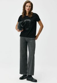 Czarny t-shirt z prostokątnym, cekinowym wzorem, szare jeansy o szerokich nogawkach, czarne loafersy oraz mała czarna torebka. Gładkie tekstury tkanin.