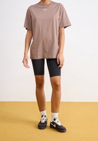 Brun bomulls t-shirt med korta ärmar och en vit Nike-logotyp, ihop med svarta cykelshorts och svarta Nike-sneakers med vita detaljer.
