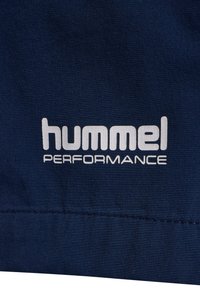 Granatowa tkanina z białym logo "hummel PERFORMANCE" umieszczonym blisko dołu, z widocznym drobnym przeszyciem.