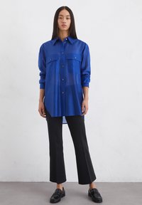 Niebieska, przezroczysta, długosleeve koszula z dwiema kieszeniami na piersi i zapięciem na guziki. Połączona z czarnymi spódnicami dzwonowymi i loafersami. Minimalistyczny design.