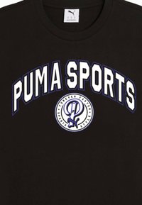 Juodas medvilninis marškinėlis su užrašu "PUMA SPORTS" ryškiu baltu šriftu su purpuriniu kontūru, centre esantis apvalus logotipas su grafikos detalėmis.