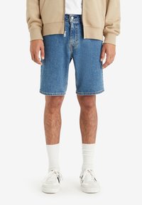 Denimshorts i ljusblått med rak skärning, avslutad fåll och framfickor. Kungsälte med vita strumpor och sneakers.