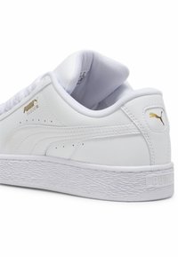 Baskets Puma Suede XL blanches montrant le côté et le talon avec le logo Puma doré, une semelle texturée et un col rembourré, sur fond blanc.