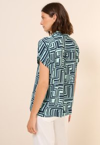 Koszula z krótkim rękawem w jasnym zielonym kolorze z geometrycznym wzorem w granatowym kolorze, z plisą z tyłu i luźnym krojem.