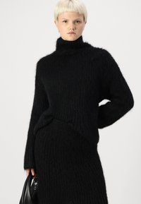 Black knitted sweater with a high neck, long sleeves, and a textured pattern. The fabric appears soft and fuzzy, creating a cozy look.