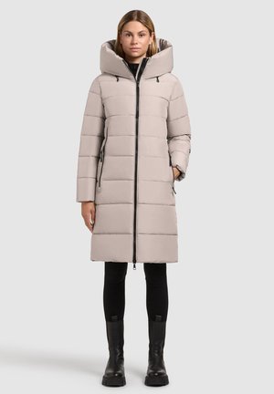 Vadderad lång kappa i ljusbeige med stor huva, framdragkedja och sidofickor. Har vertikala sömmar och svarta detaljer.