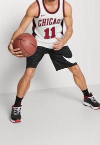 Un joueur de basket-ball portant un maillot blanc de Chicago avec des accents rouges, un short noir avec un motif blanc et des baskets noires avec des détails rouges.