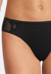 Schwarze Bikini-Unterhose mit einem glatten, elastischen Bund und einem Netzspitzenpaneel auf einer Seite, verziert mit floralem Muster.