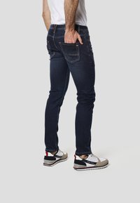 Mørkeblå jeans med tætsiddende pasform, diskrete slidmærker og fem lommer. Kombineret med hvide, grå og røde sportssko.