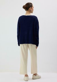 Tmavomodrý sveter so širokým strihom, s krémovým okrúhlym výstrihom. Kombinovaný s krémovými širokými nohavicami a svetlými teniskami. Hladká textúra.