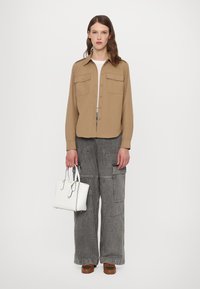 Beige skjorte med knapper og brystlommer, grå vide cargo-bukser, hvit håndveske og brune sko. Glatt stoff med et avslappet design.