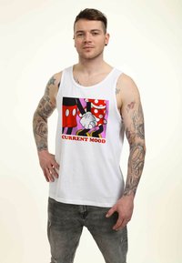 Camiseta de tirantes blanca con un gráfico colorido que presenta lunares rojos, detalles negros y el texto "ESTADO ACTUAL" en rojo. Combinada con jeans grises desgastados.