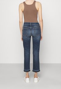 Jeans in denim scuro con silhouette aderente, orli sfrangiati e due tasche posteriori. Abbinati a una canotta a costine marrone e scarpe bianche.