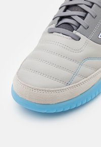 Grå lädersneaker med sömnadsdetaljer, ljusblå accenter och en texturerad grå mocka tåhätta. Utrustad med en ljusblå gummisula.