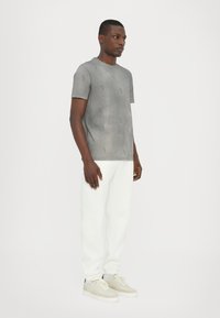 Grå kortærmet T-shirt med subtilt logomønster. Bæres med hvide sweatpants og lysegrå sneakers. Glat tekstur, afslappet pasform.