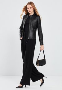 Black leather jacket with a fitted design, zippered pockets, paired with black wide-leg pants and pointed high heels. Includes a small black handbag.
