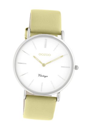 Silver metal watch with a white dial, yellow hands, and a green leather strap. Features minimalist hour markers and "Vintage" text.