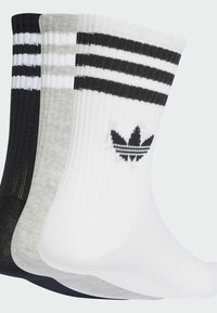 Trzy pary skarpet sportowych w kolorze czarnym, szarym i białym. Każda z nich ma prążkowaną teksturę i białe paski, a biała para dodatkowo posiada logo Adidas.