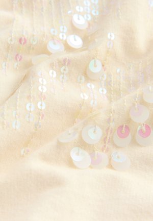 Tissu crème orné de sequins circulaires irisés cousus en lignes verticales, créant texture et scintillement sur toute la surface.