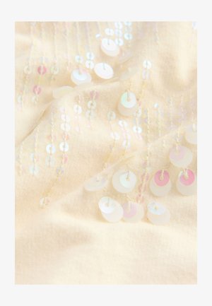 Kremna tkanina z irizirajočimi krožnimi bleščicami, všitimi v navpičnih linijah, ki ustvarjajo teksturo in bleščice po celotni površini.