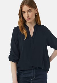 Granatowa bluzka z dekoltem w kształcie litery V i krótkimi, podwiniętymi rękawami. Miękka, gładka tkanina o luźnym kroju, zestawiona z ciemnymi dżinsami.